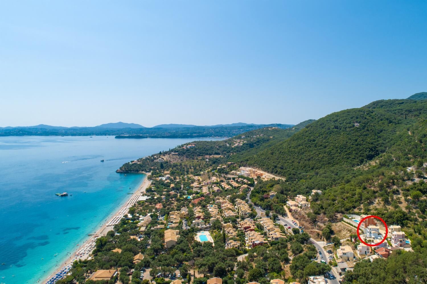 An aerial view of a coastal town with a beach, houses, and a pool area.