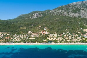 A coastal town with buildings along the beach and a mountain in the background. - Villa Alya View in Mparmpati (Corfu)