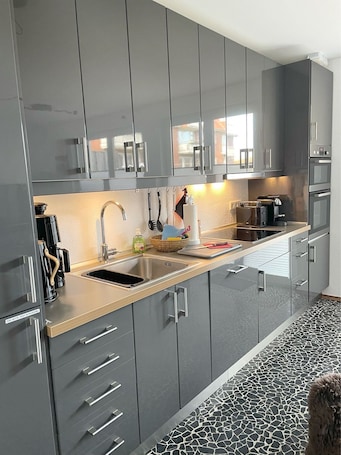 A modern kitchen with grey cabinetry, stainless steel appliances, and a tiled backsplash.