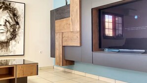 Un salon moderne avec un téléviseur à écran plat fixé sur un mur bleu, un meuble TV en bois et un grand tableau abstrait.