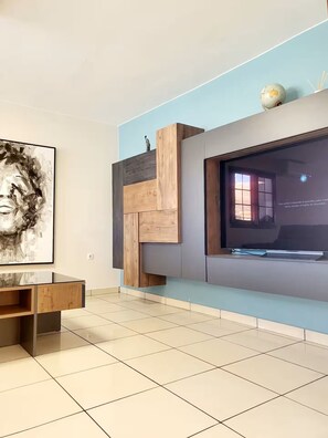Ein modernes Wohnzimmer mit einem flachbildfernseher an einer blauen Wand, einem Holz-Fernsehschrank und einem großen abstrakten Gemälde.