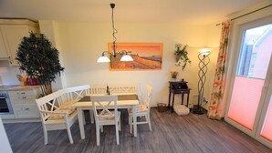 A dining area with a white table and chairs, a painting on the wall, a potted plant, and a floor lamp. - DUE/09, Apartment 15 - Im Dünengrund App. 14 and 15 (Sylt)