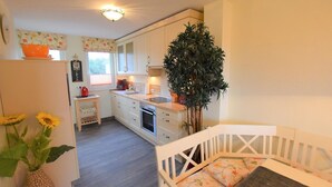 A compact kitchen with white cabinets, a built-in oven, and a small dining area with a white table and bench. - DUE/09, Apartment 15 - Im Dünengrund App. 14 and 15 (Sylt)