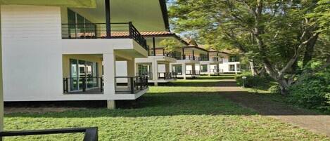 A modern multi-story building with balconies, a well-maintained lawn, and surrounding trees.