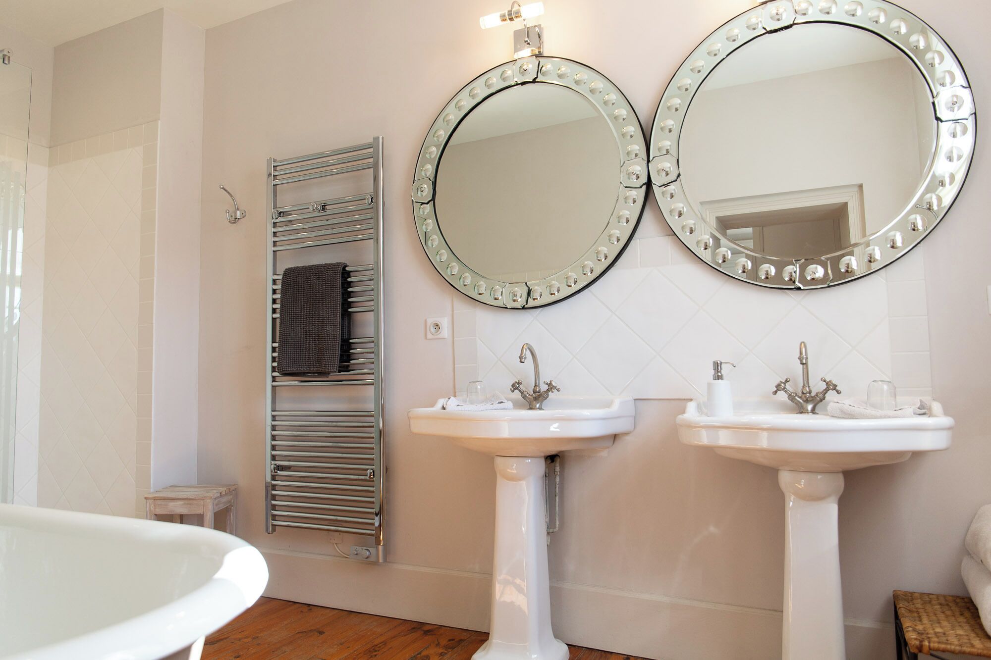 A bathroom with two sinks, a towel rack, and two mirrors with lights.