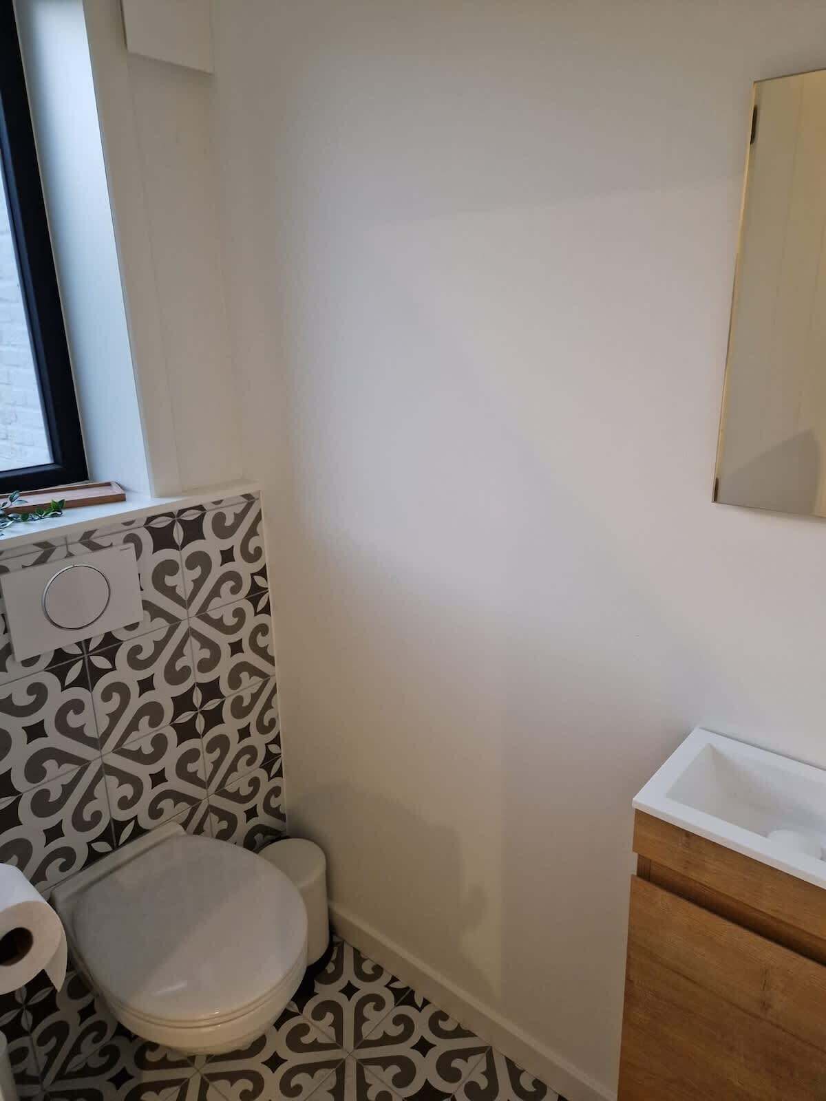 Ein kleines Badezimmer mit Toilette, Waschbecken und Wandfliesen mit Muster.