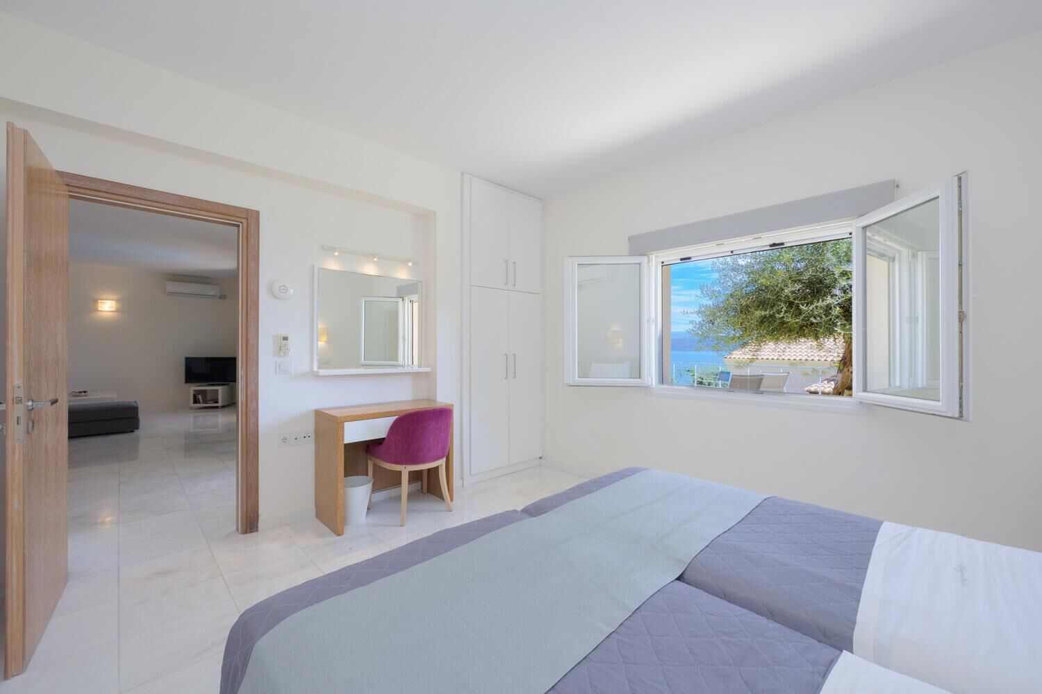 A bedroom with a bed, a desk, a chair, a mirror, and a window with a view of the outdoors.