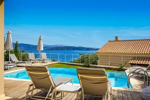 A poolside area with lounge chairs, a pool, and a view of the sea and mountains. - Villa Odysseus in Ionian Islands (Corfu)