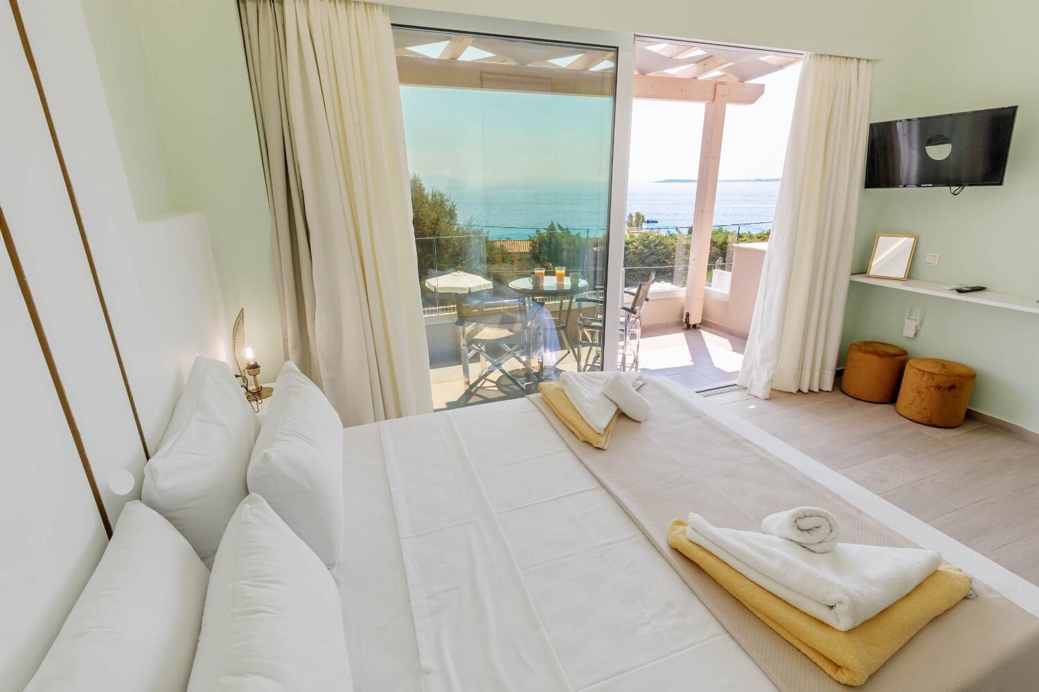 Ein Hotelzimmer mit einem großen Bett, einem an der Wand befestigten Fernseher und einem Balkon mit Meerblick.