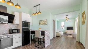 A modern kitchen with a refrigerator, microwave, and stove. There is a dining area with a table and chairs. The room has light green walls and wooden flooring. - Villa Stavroula in Mparmpati (Corfu)