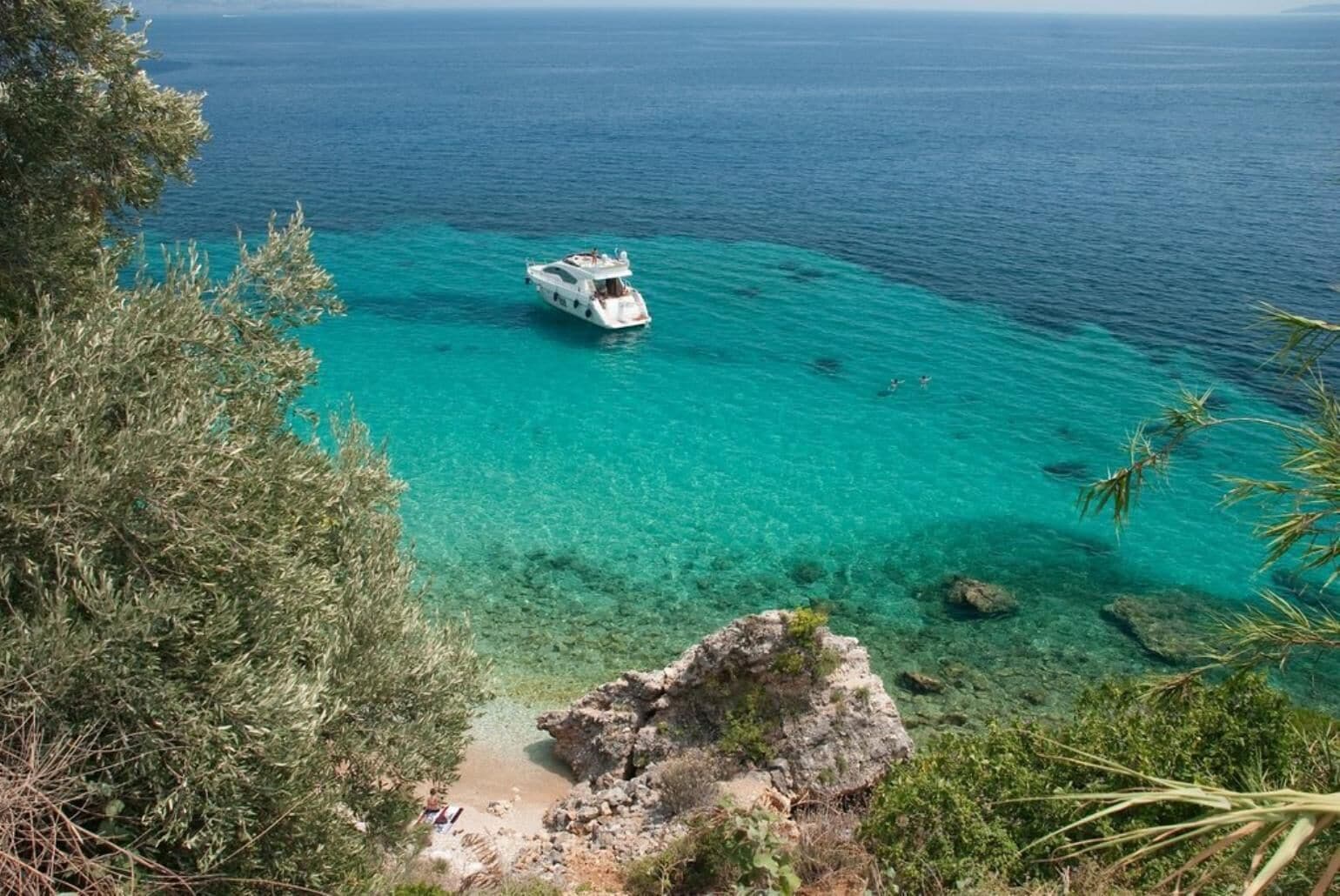 A boat on clear turquoise waters with rocky terrain and dense vegetation.