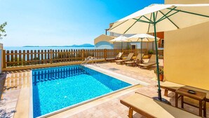 A pool area with a wooden fence, lounge chairs, and umbrellas. - Villa Sequoia Yellow (Corfu)