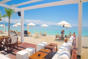 Un patio frente a la playa con asientos al aire libre, sombrillas y vista al mar.