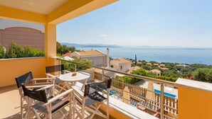 A balcony with a table and chairs, overlooking a coastal view with houses and a clear sky. - Villa Sequoia Yellow (Corfu)