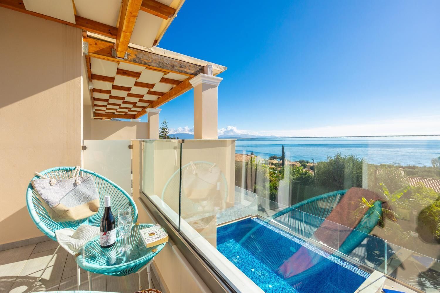 A balcony with a glass railing overlooking a pool and a clear view of the sea.