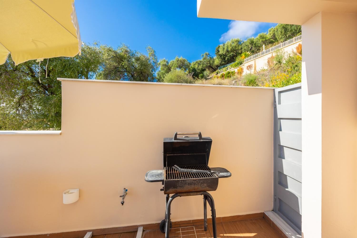 Un pequeño espacio al aire libre con una parrilla, una ventana y un paraguas amarillo.