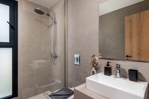 A modern bathroom with a glass-enclosed shower, a white sink with a black soap dispenser, and a wooden cabinet above the mirror. - Villa Salty Sun 5 in Kremasti (Rhodes)