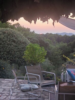 An outdoor seating area with two lounge chairs and a small table, surrounded by lush greenery and a view of distant hills.