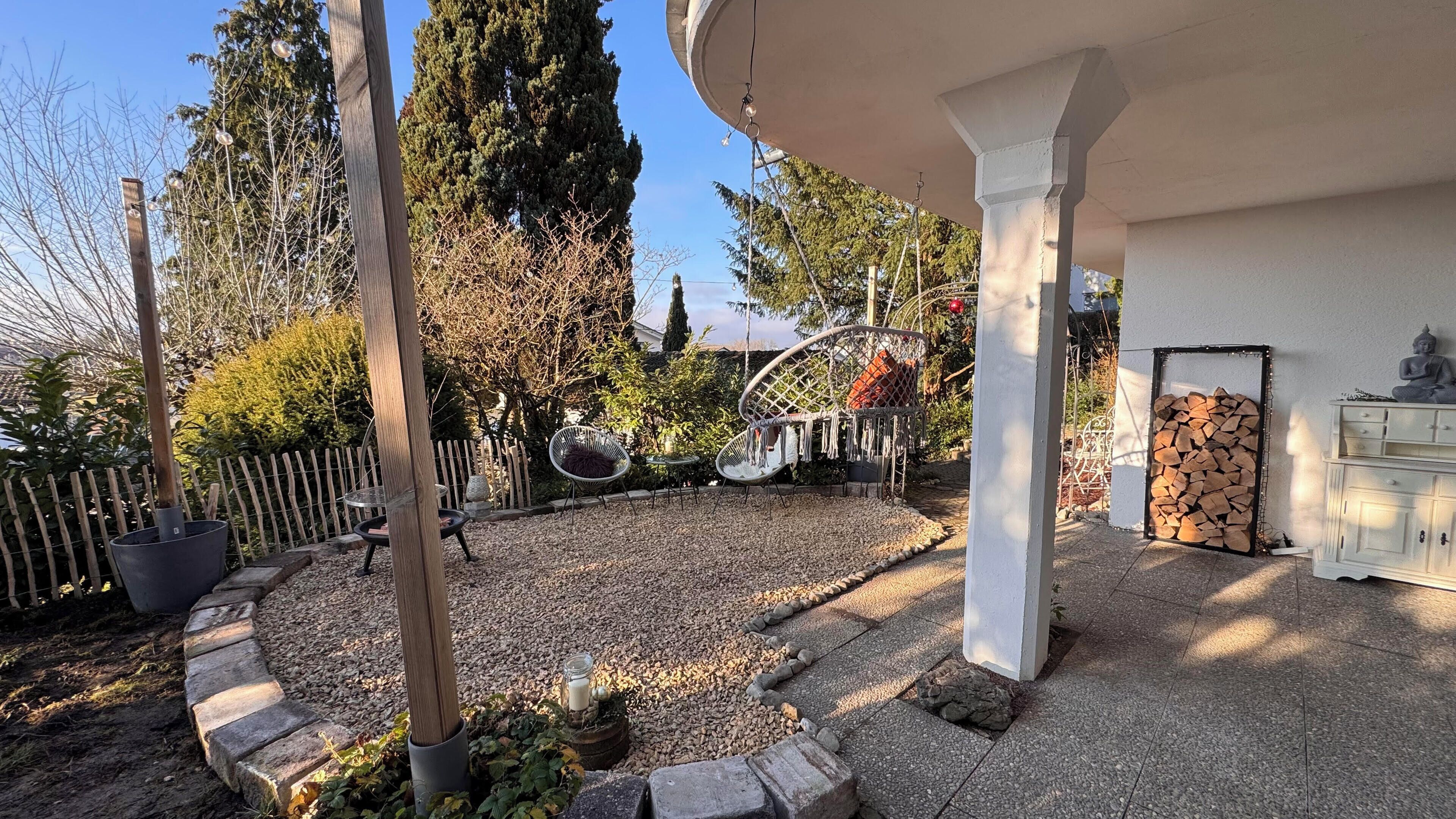 A garden patio with a pergola, outdoor seating, and a stone fireplace.