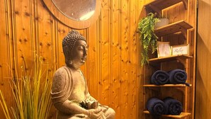 Eine Statue eines sitzenden Bildes, ein Spiegel, ein Regal mit Handtüchern und ein Korbwicker-Korb auf einem gefliesten Boden.