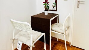Ein kleiner Raum mit Holzboden, einer weißen Tür, einer weißen Wand, einem braunen Tisch, zwei weißen Stühlen und einem Spiegel an der Wand.