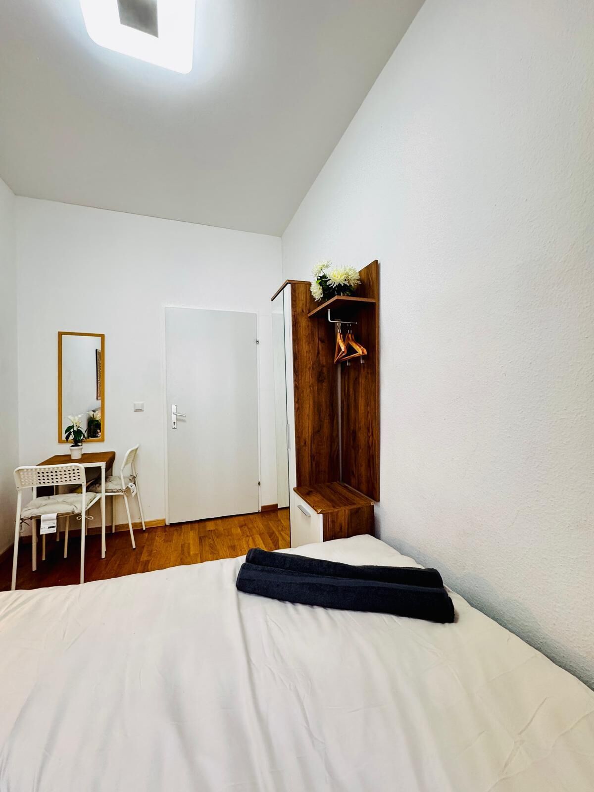 A bedroom with a bed, a desk with a chair, a wardrobe, and a mirror.