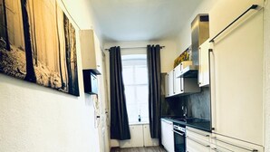 Eine schmale Küche mit Holzboden, weißen Schränken und einem Fenster mit Vorhängen.
