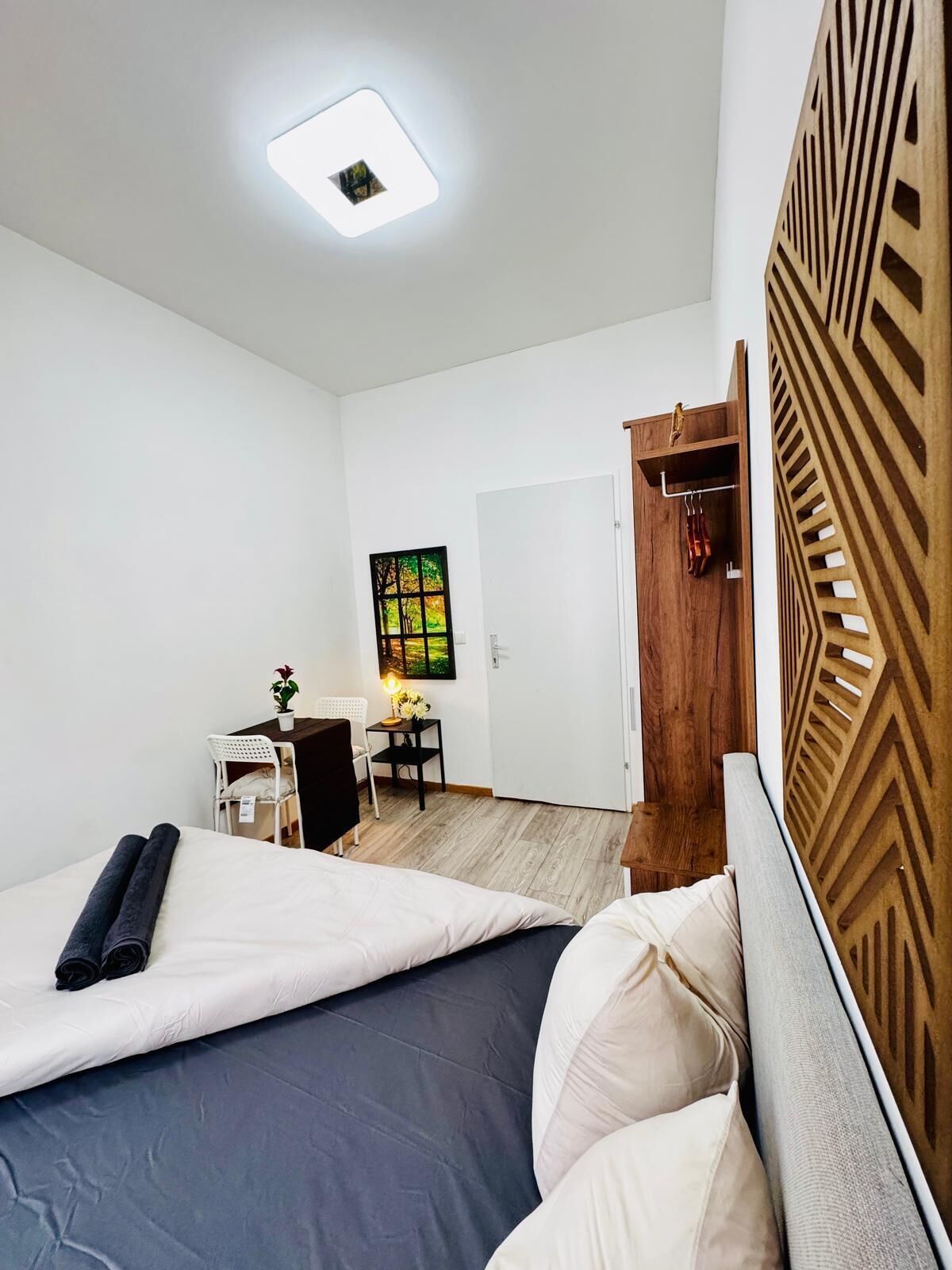 Een moderne hotelkamer met twee bedden, een houten hoofdeinde, een klein bureau met stoel, een schilderij aan de muur en een deur die naar een andere kamer leidt.