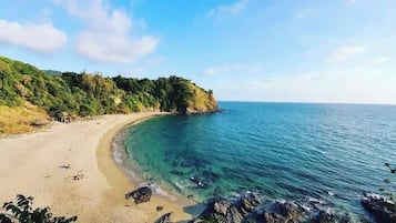 A coastal beach with clear blue waters, sandy shore, and a forested cliff.
