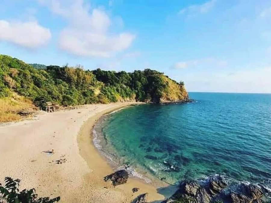 Una playa costera con aguas azules cristalinas, orilla arenosa y un acantilado arbolado.