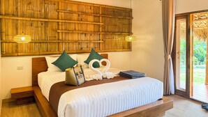 Uma cama com estrutura de madeira, duas almofadas verdes, uma almofada em forma de cisne branco, uma bolsa tecida e uma toalha dobrada.