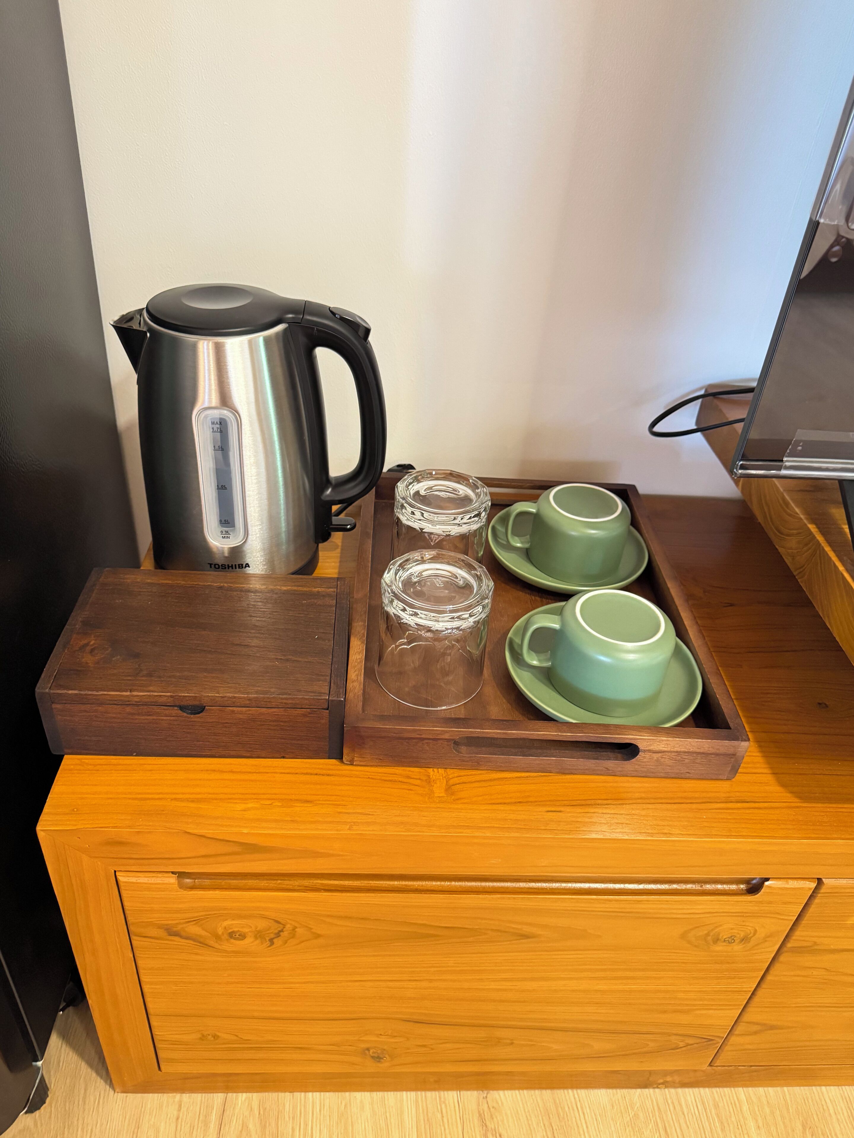 A wooden drawer with a tray containing a stainless steel kettle, two clear glass cups, and a green cup and saucer.