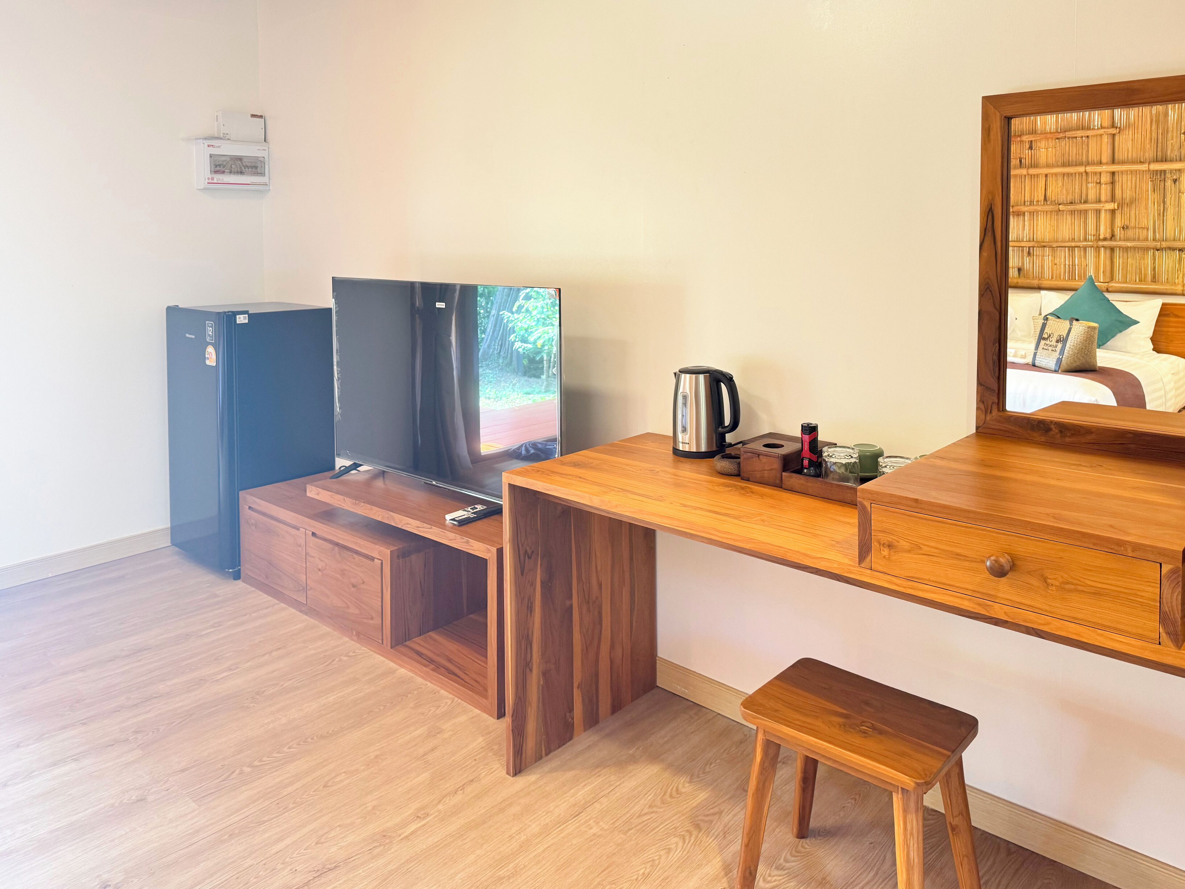 Een knus ingerichte kamer met een houten bureau, een televisie, een kleine koelkast en een houten kruk.