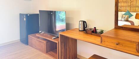 Een knus ingerichte kamer met een houten bureau, een televisie, een kleine koelkast en een houten kruk.