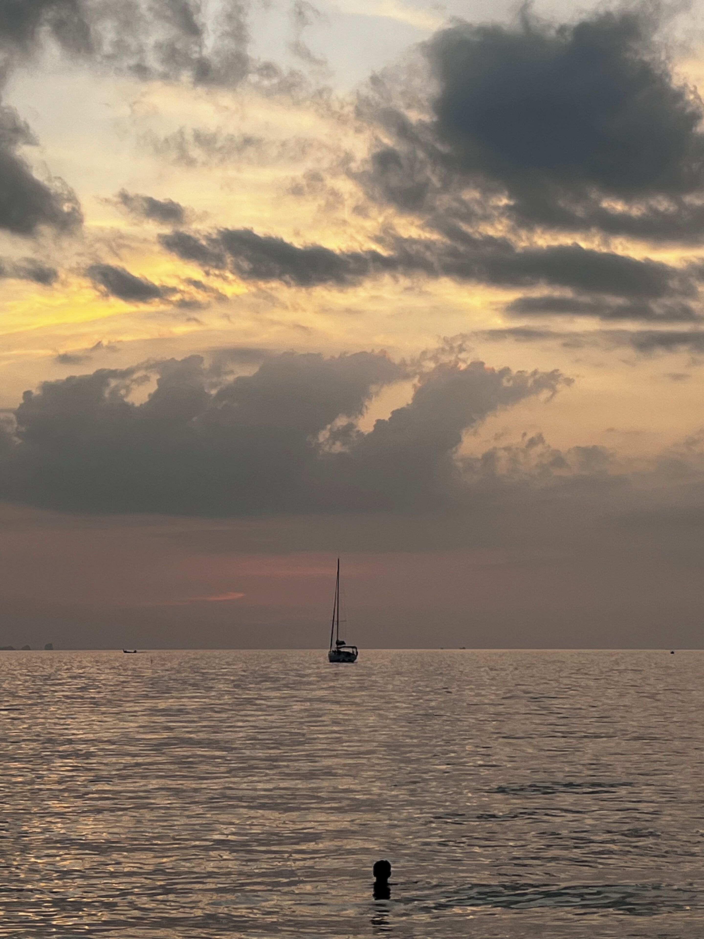 A calm sea with a sailboat in the distance, under a cloudy sky.