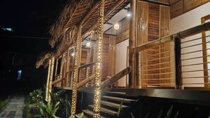 Uma construção com telhado de palha, paredes de madeira e uma escada que leva a um andar superior.