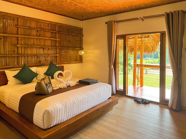 A bedroom with a large bed, green pillows, a heart-shaped towel, and a view of a garden through a sliding door. - Painon Resort KohLanta (Ko Lanta)