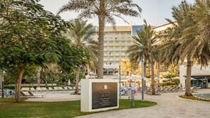 A hotel courtyard with palm trees, lounge chairs, and a sign indicating 'Address Residences Fujairah'. - 3BR Family Residence w/ Distant Sea View and Assistant Room, Near to Beach (Fujairah)