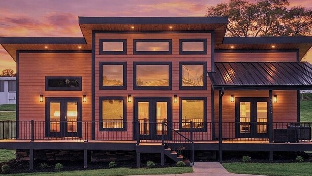A modern two-story house with a flat roof, large windows, and a covered porch.