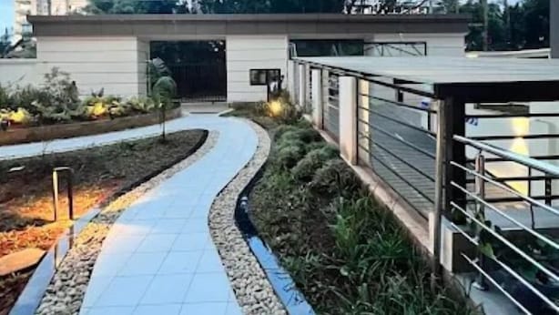 Een modern gebouw met een overdekte doorgang, een betegeld pad en aangelegde gebieden met planten en grind.