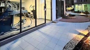 Een modern gebouw met een glazen gevel, een fitnessruimte met trainingsapparatuur, en een aangelegde buitenruimte met een waterpartij.