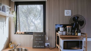 Eine kleine Küche mit Spüle, Mikrowelle, einem Tisch mit Geschirr, einem Ventilator und einem Willkommensschild.