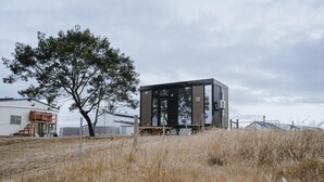 Ein modernes, modulares Gebäude mit Metallfassade, gelegen in einer grünen Wiese mit einem großen Baum in der Nähe.