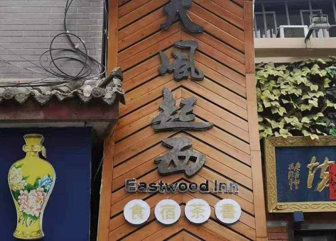 Ein Hotel Schild mit Eastwood Inn und chinesischen Schriftzeichen, einer dekorativen Vase und einer mit Efeu bewachsenen Wand.