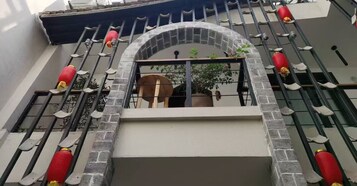Varanda com arco de pedra, vasos de plantas e lanternas vermelhas.