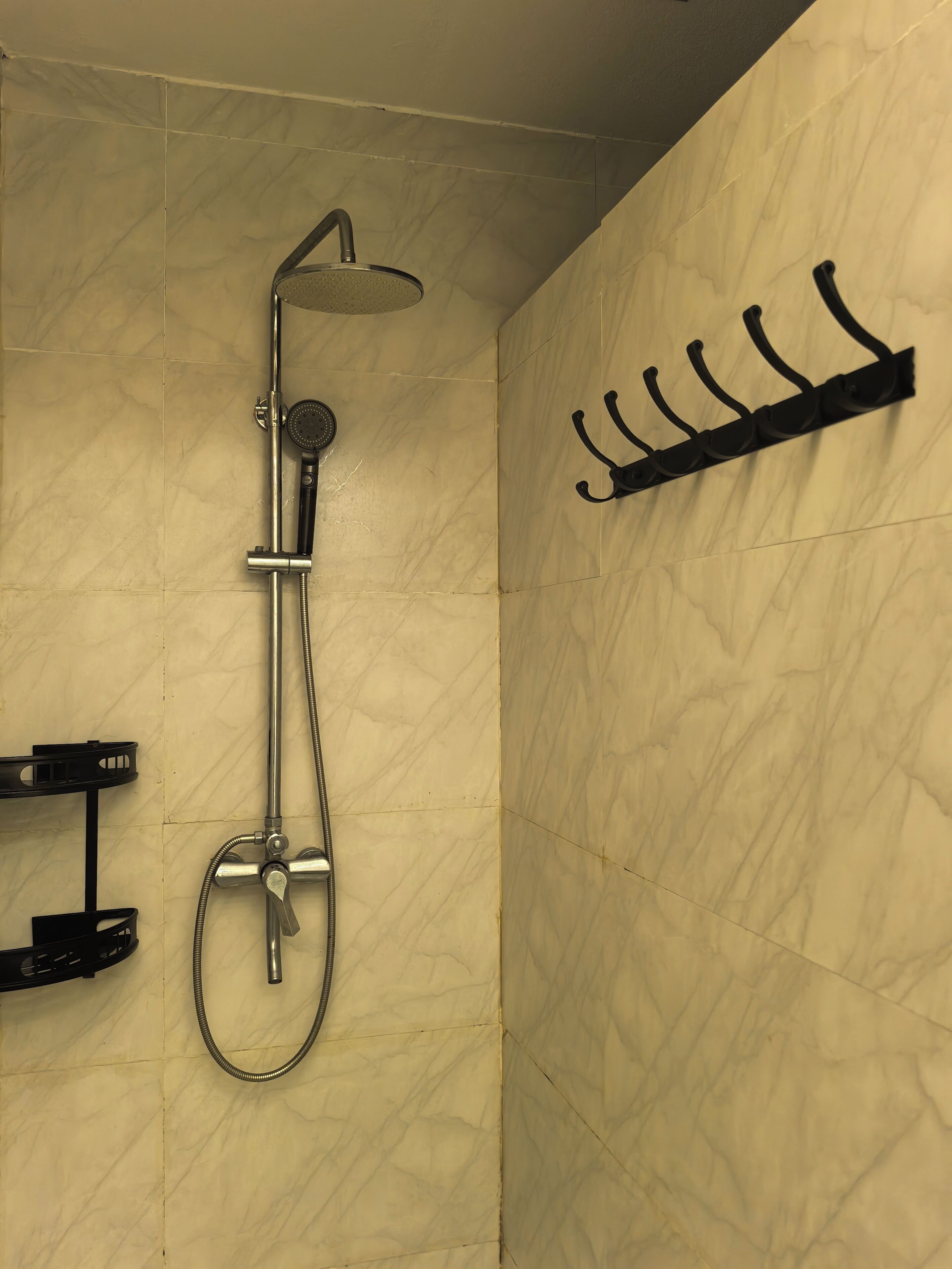 A bathroom with a shower, a towel rack, and a shelf with toiletries.
