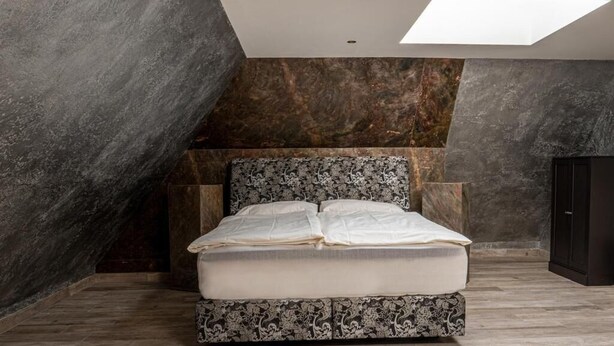 Une chambre moderne avec un grand lit, des murs en pierre sombre et une lucarne.