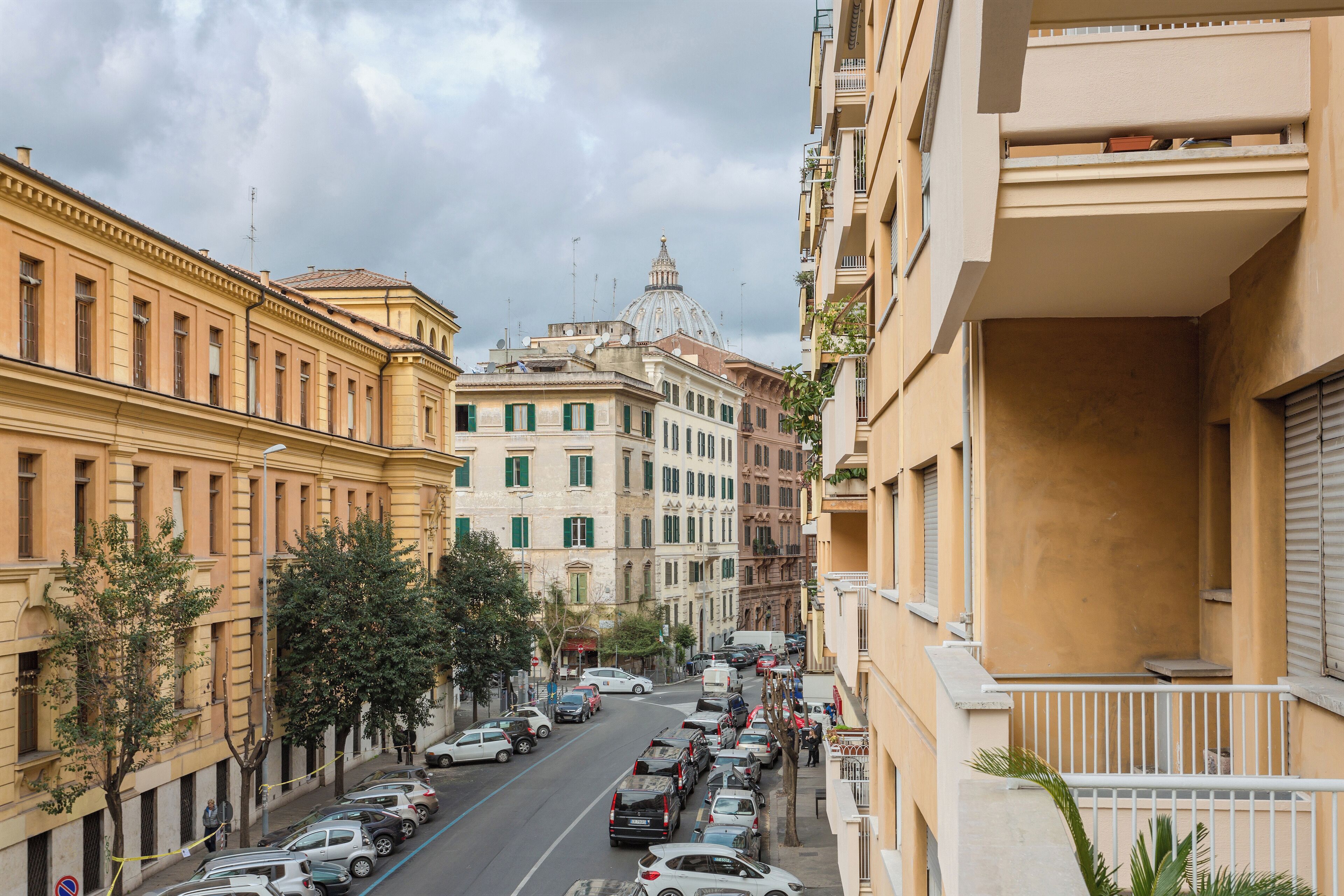 A street view with parked cars, buildings, and a dome structure in the background.