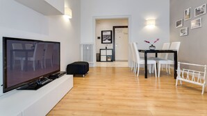 Un salon moderne avec un téléviseur à écran plat, une table à manger avec des chaises et un banc blanc.