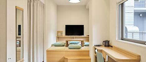 A narrow hotel room with a bed, a TV, a desk, and a window.